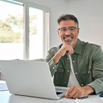 Man with glasses smiling while working on laptop