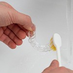 Patient using toothbrush to clean aligner