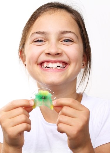 Smiling young girl holding an orthodontic appliance