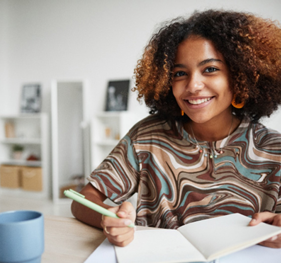 Teen smiling while taking notes at home