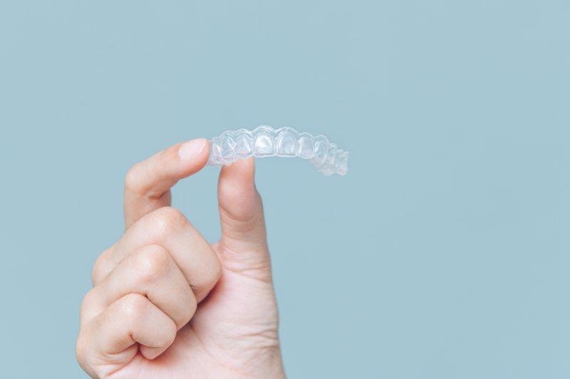 Hand holding a clear aligner over blue background