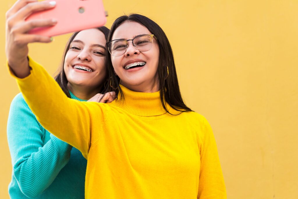 A woman and teen with braces smiling taking selfie with yellow background